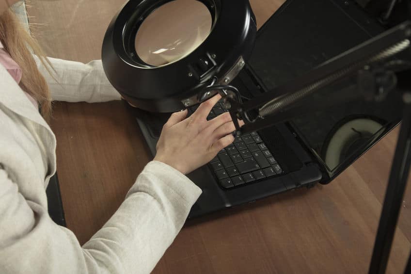 business woman looking into magnifier to see computer keyboard